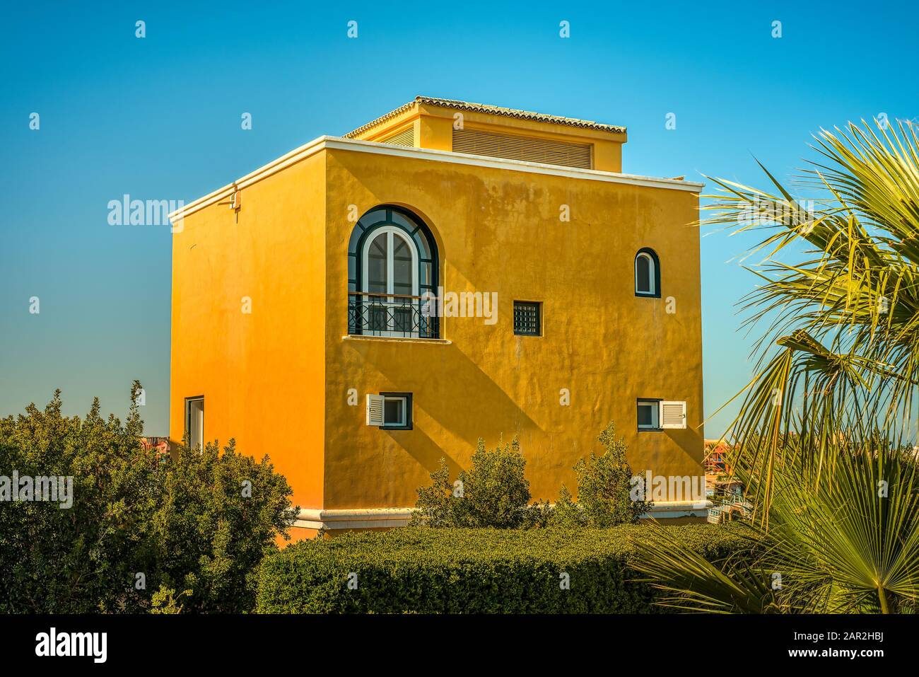 Ein quadratisches gelbes Haus unter den Palmen im Sonnenschein gegen einen blauen Himmel, El Gouna, Ägypten, 12. Januar 2020 Stockfoto