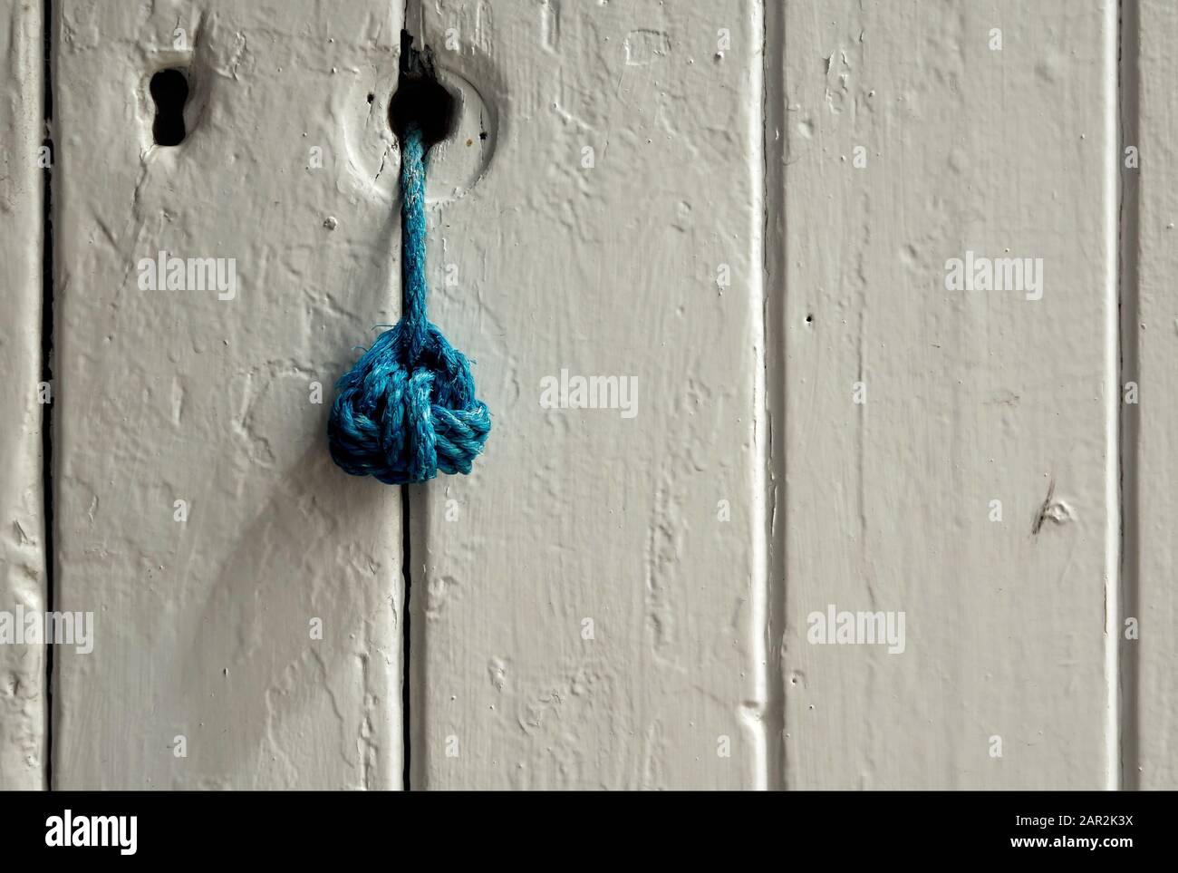 Abstrakte Ansicht der verwitterten, weiß lackierten Zungen- und Rillentür mit Schlüsselloch und blauem Türzug Stockfoto