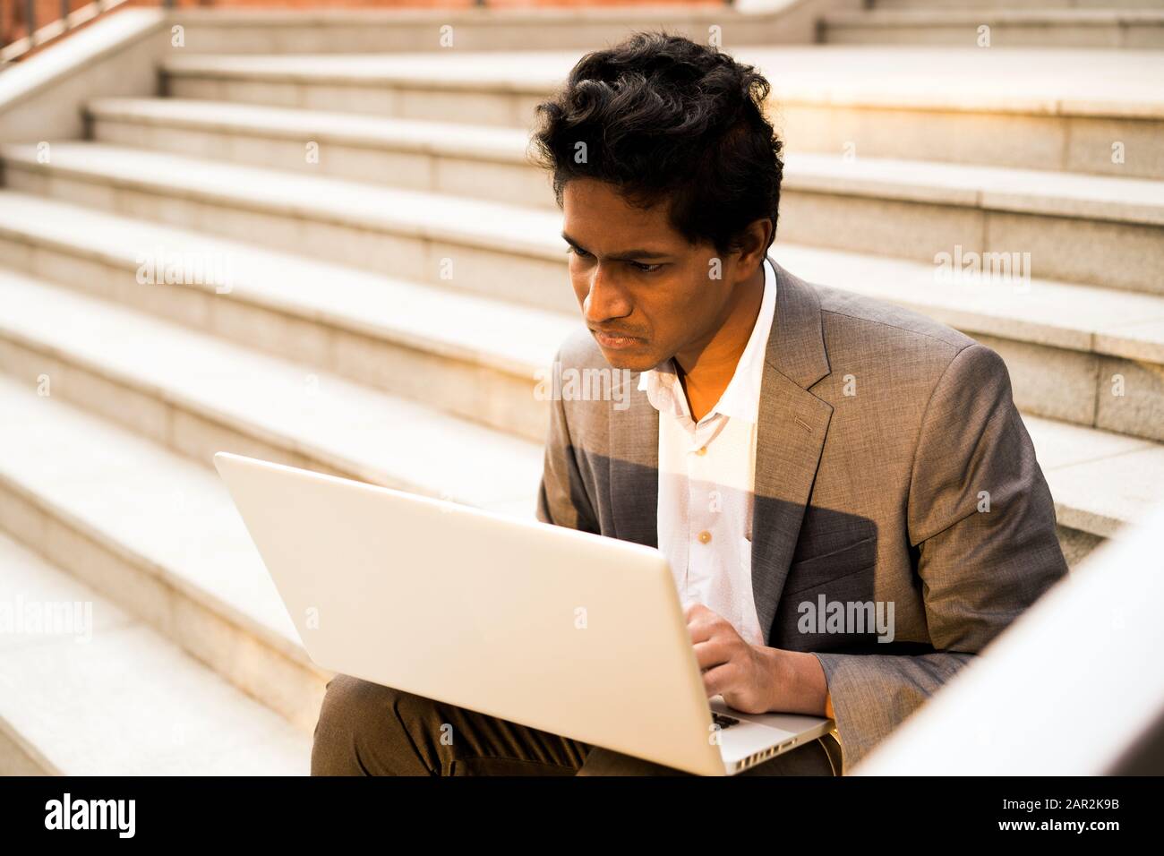 Junge schöne Indische Mann sitzt mit einem Laptop, lächelnd und Eingabe Stockfoto