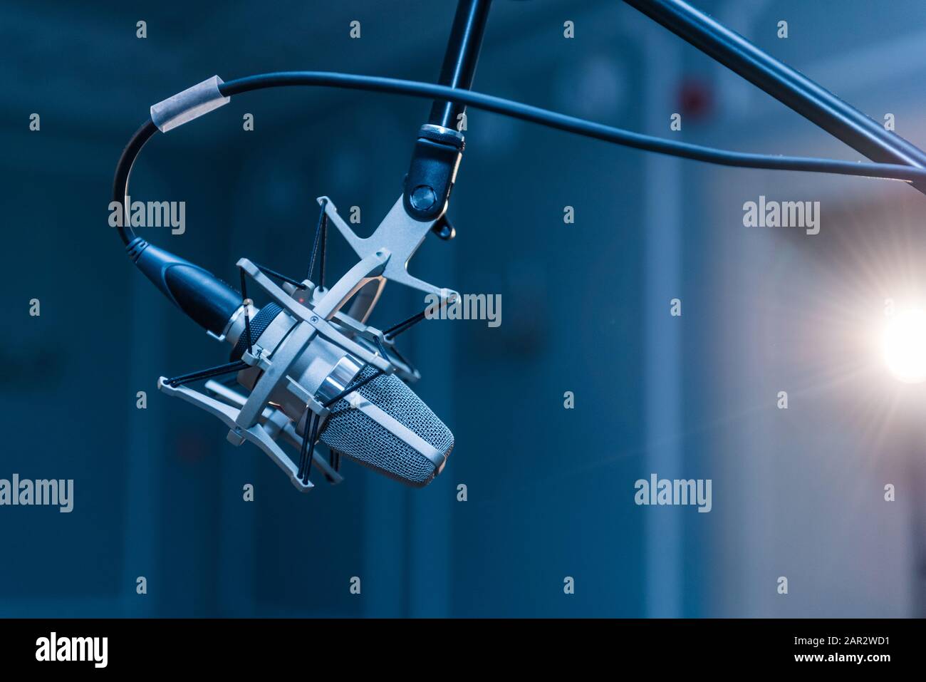 Ein professionelles silbernes Kondensatormikrofon, das auf einem schwarzen Stativ montiert ist und in einem Konzertsaal mit Punktbeleuchtung aufgestellt ist. Stockfoto