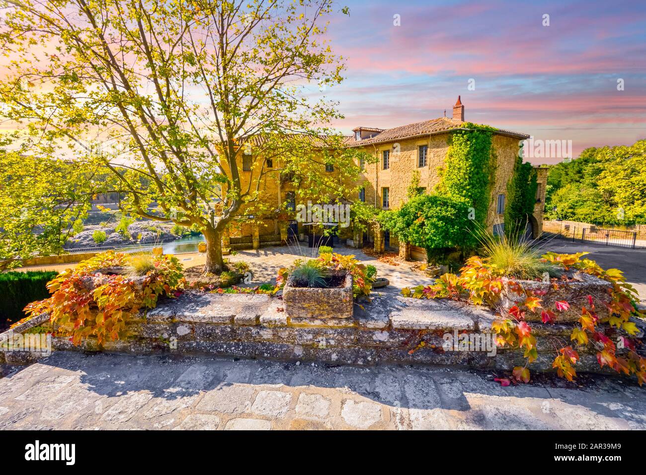 Ein farbenfroher Himmel und Sonnenuntergang über einem historischen Stuck- oder Landsitz entlang eines Flusses im südfranzösischen Gebiet der Provence im Herbst. Stockfoto