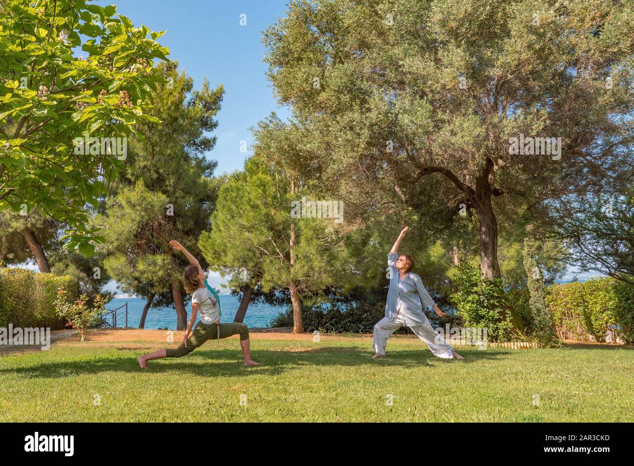 Yoga, Krieger-Pose. Zwei Frauen machen Yoga auf dem Hinterhof, vor dem Hof. Gesundes Lifestyle-Konzept. Morgens körperliche Aktivitäten im Park, Hinterhof. Glückliche Frauen kümmern sich um ihren Körper. Stockfoto