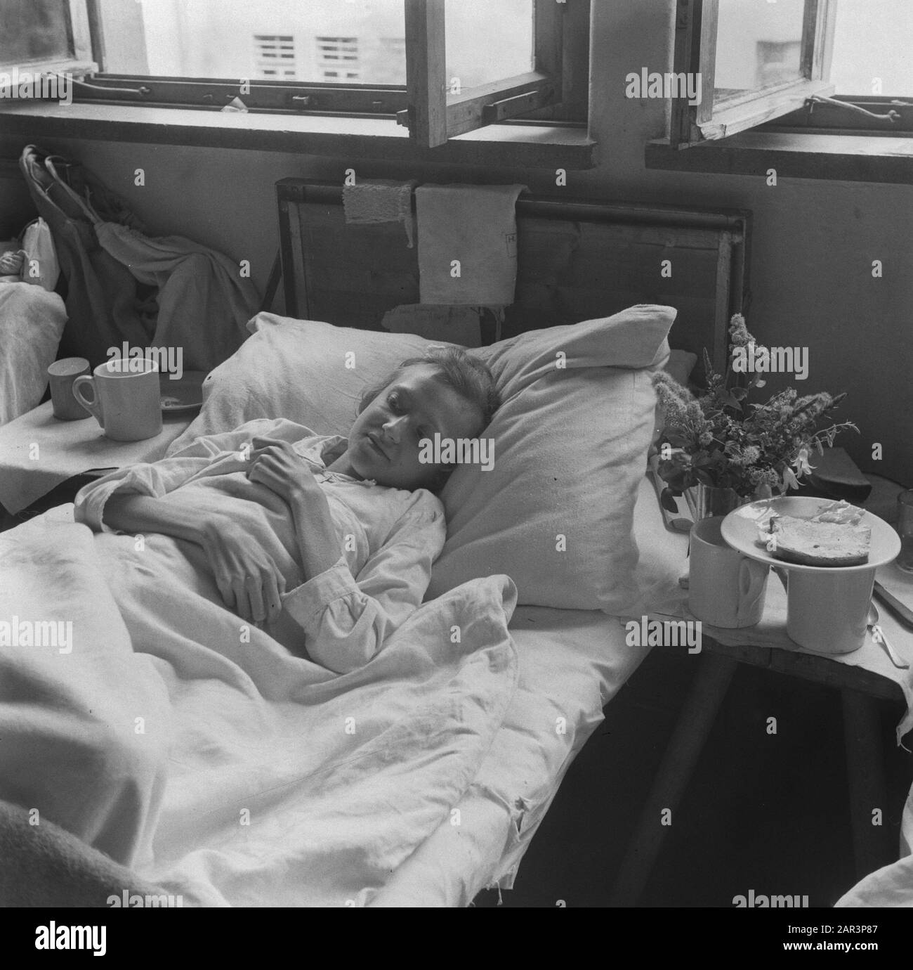 Rückkehrlager Bergen-Belsen Frau liegt im Bett neben ihren Trinkbecher und einem Teller mit Brotdatum: 1945 Ort: Bergen-Belsen, Deutschland Schlagwörter: Konzentrationslager, Rückführung, zweiter Weltkrieg, Frauen Stockfoto