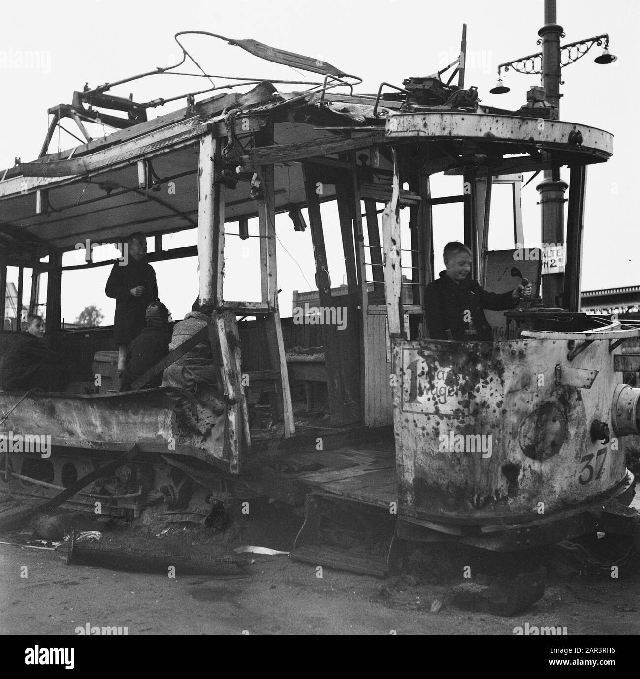 Erholung: Arnhem [Kinder, die in einer zerstörten Straßenbahn spielen] Anmerkung: Die Straßenbahn steht in der Nähe eines Lampenpfostens mit der Beschilderung Haltestelle 2. Gelderland Schlagwörter: Kinder, Straßenbahnen, Verwüstungen, Wiederaufbau Stockfoto