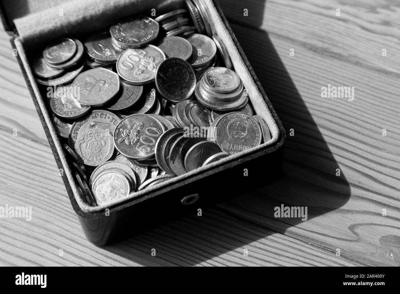 Graustufen-High-Angle-Aufnahme einer Box voller Münzen auf einer hölzernen Oberfläche Stockfoto