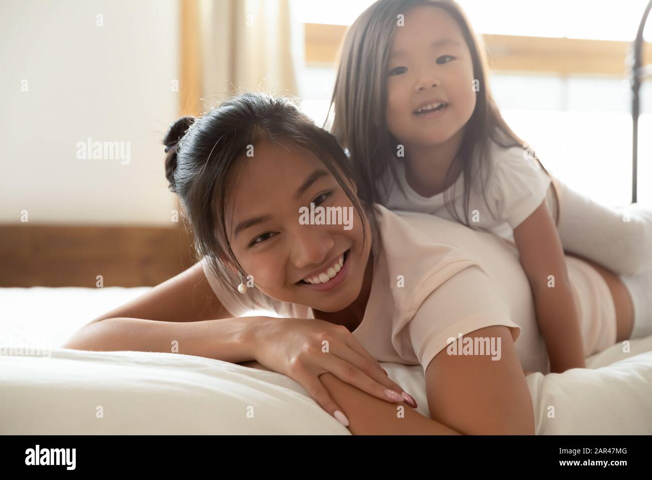 Glückliche asiatische Mutter und kleine Tochter kuscheln im Bett Stockfoto