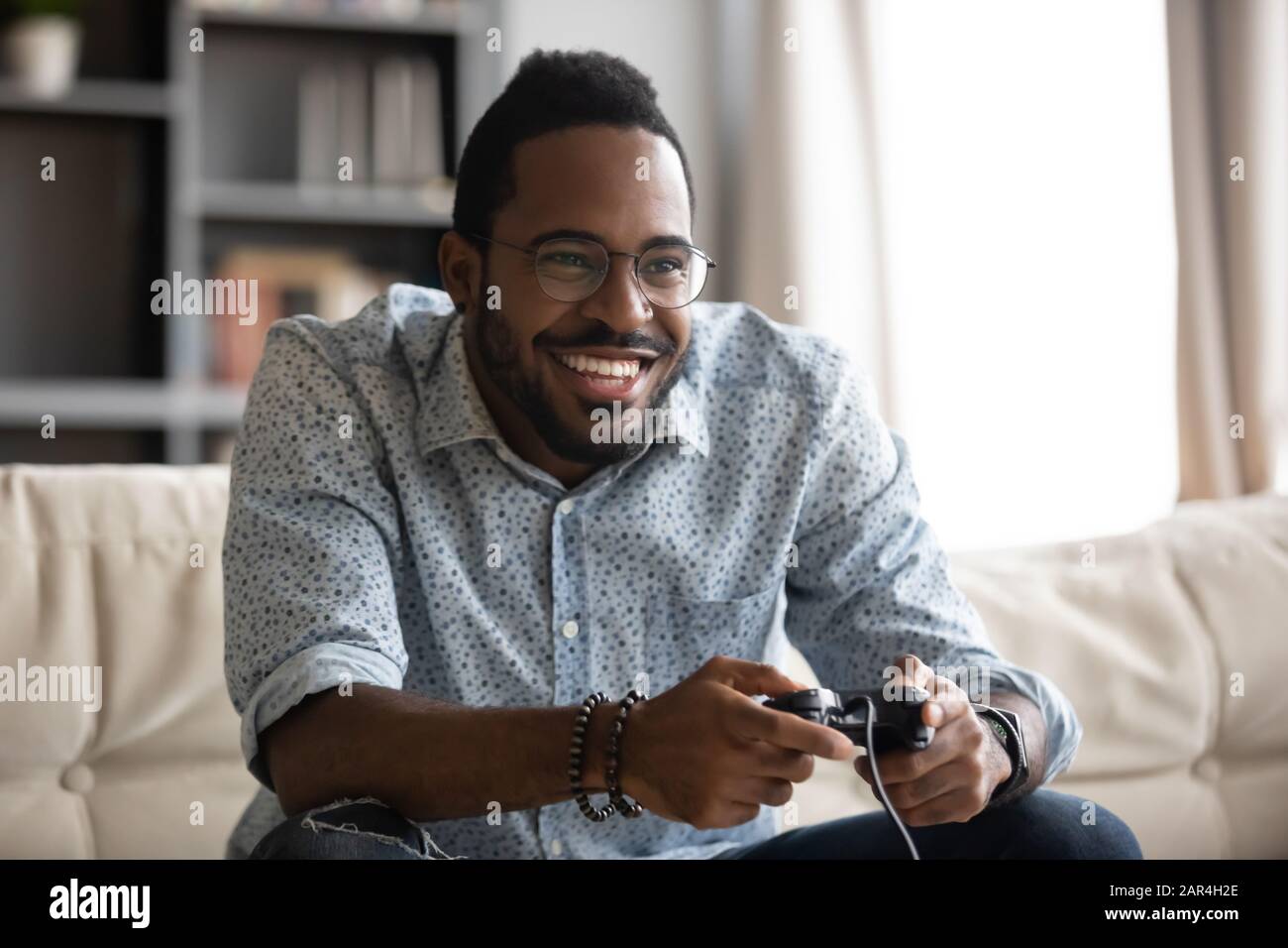 Fröhlicher junger afrikanischer Kerl, der Joystick-Controller hält, der Videospiel spielt Stockfoto