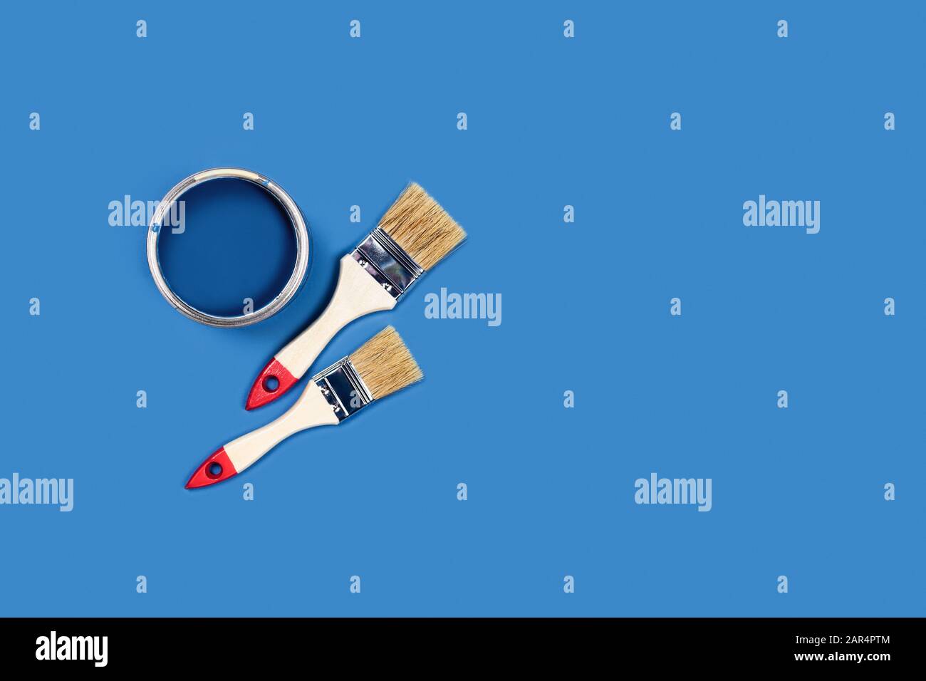 Foto für Wohnungsreparaturen. Blauer Hintergrund mit Farbkisten und zwei Holzquasten. Stockfoto