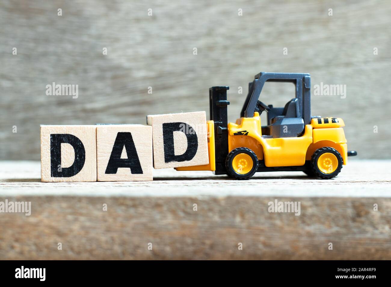 Der Gabelstapler von Toy hält den Buchstabenblock d, um das Wort "Papa" auf dem Holzhintergrund fertigzustellen Stockfoto