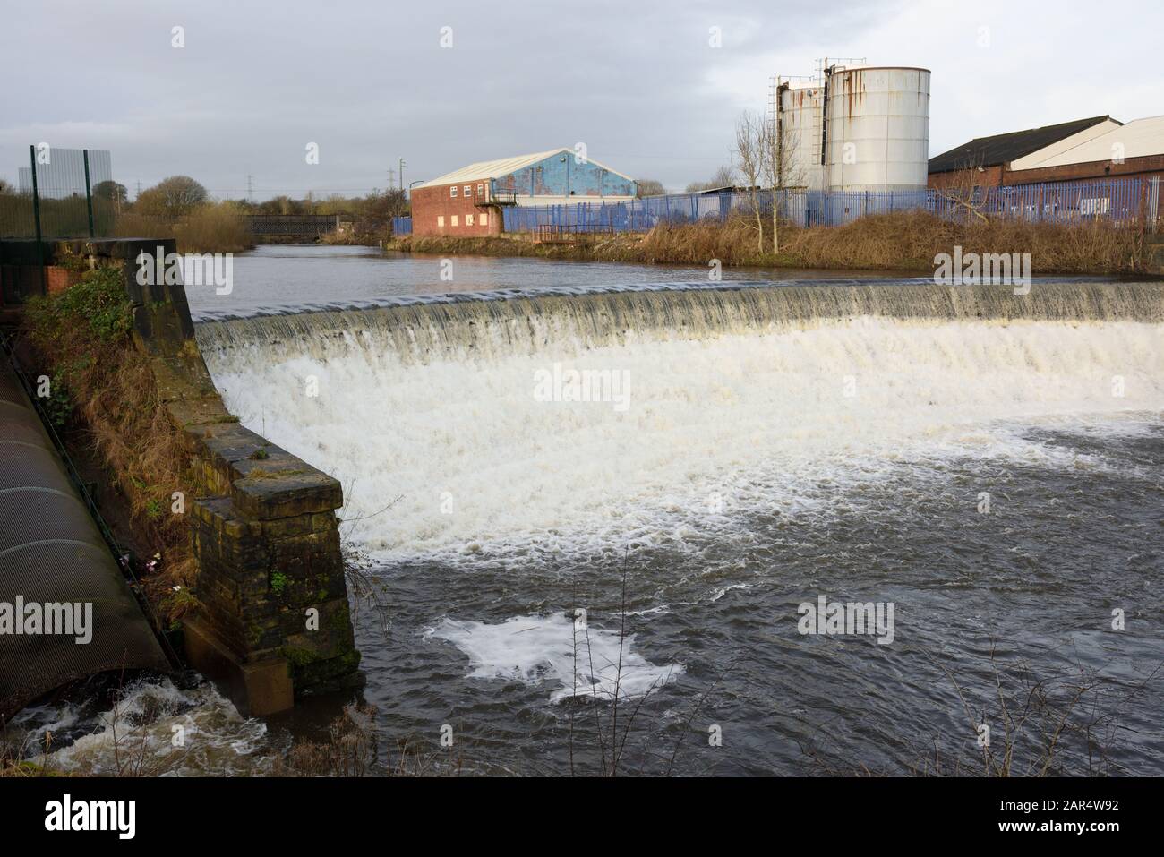 Weir am Fluss irwell mit Industriegebäuden und Silos im Hintergrund in Bury lancashire UK Stockfoto