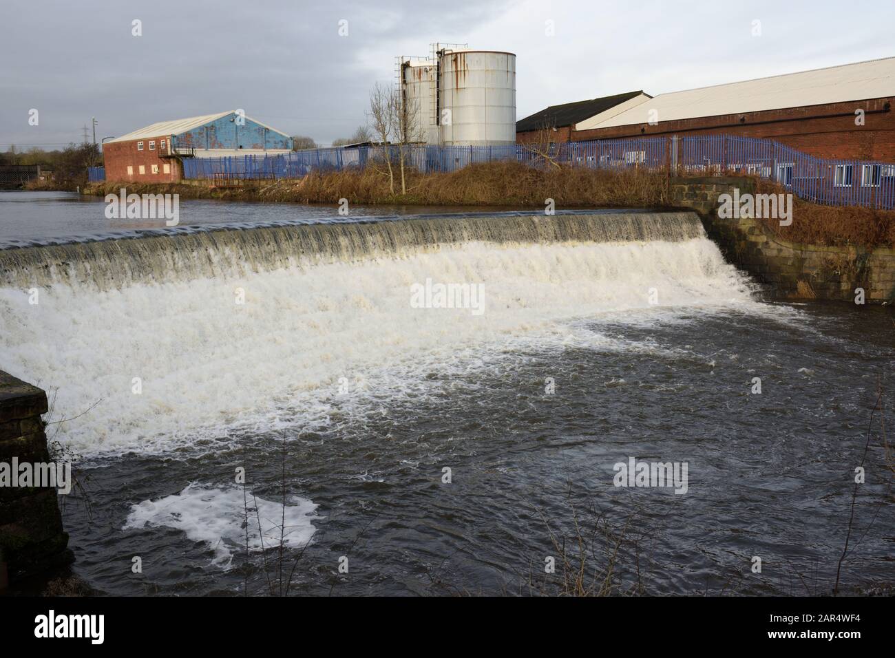 Weir am Fluss irwell mit Industriegebäuden und Silos im Hintergrund in Bury lancashire UK Stockfoto