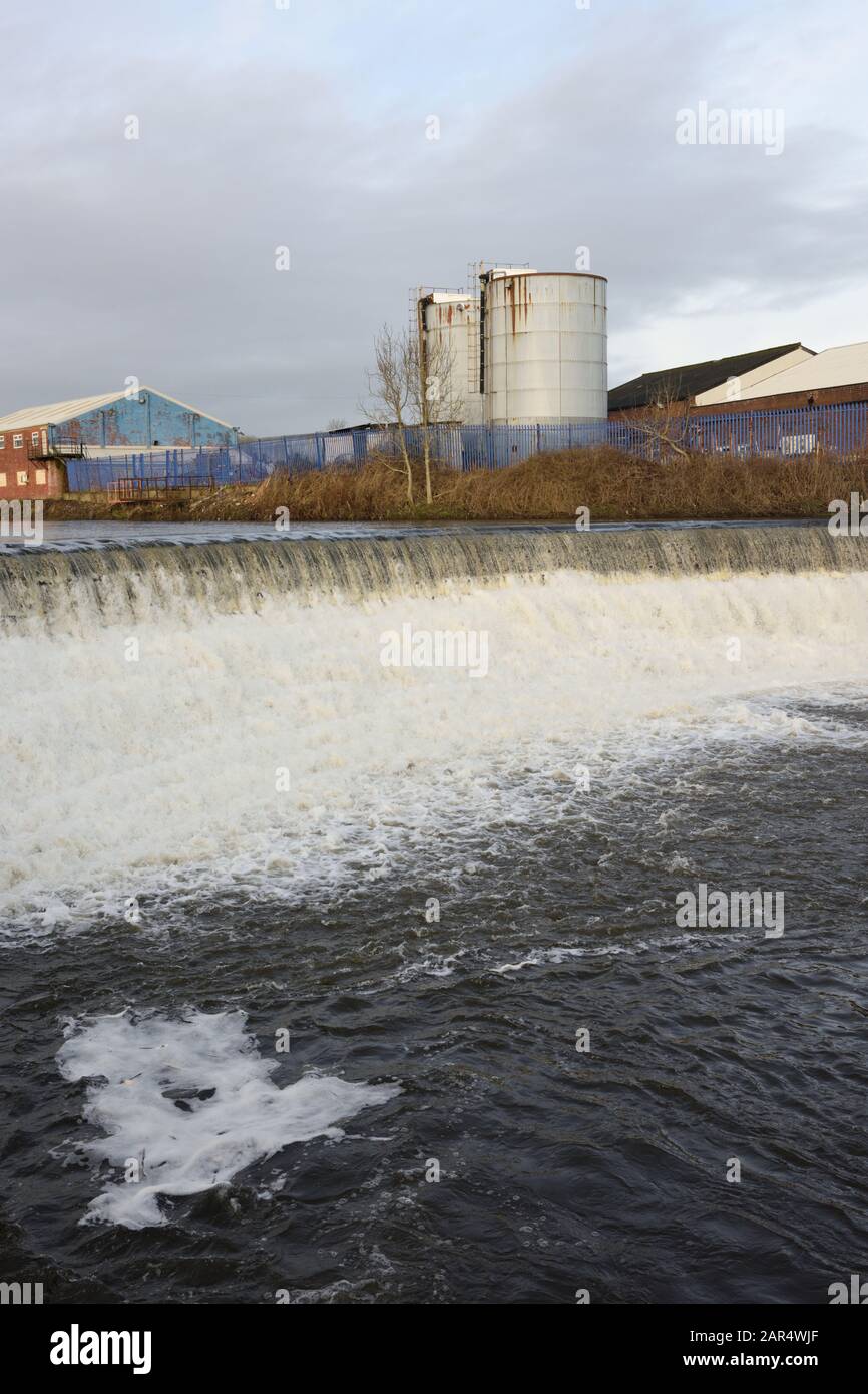 Weir am Fluss irwell mit Industriegebäuden und Silos im Hintergrund in Bury lancashire UK Stockfoto