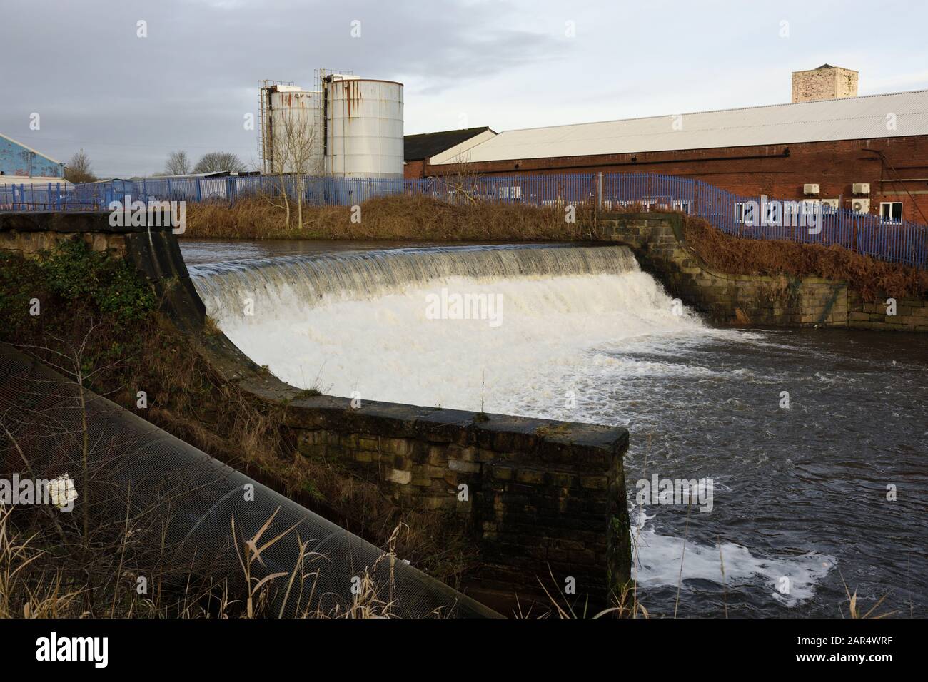 Weir am Fluss irwell mit Industriegebäuden und Silos im Hintergrund in Bury lancashire UK Stockfoto