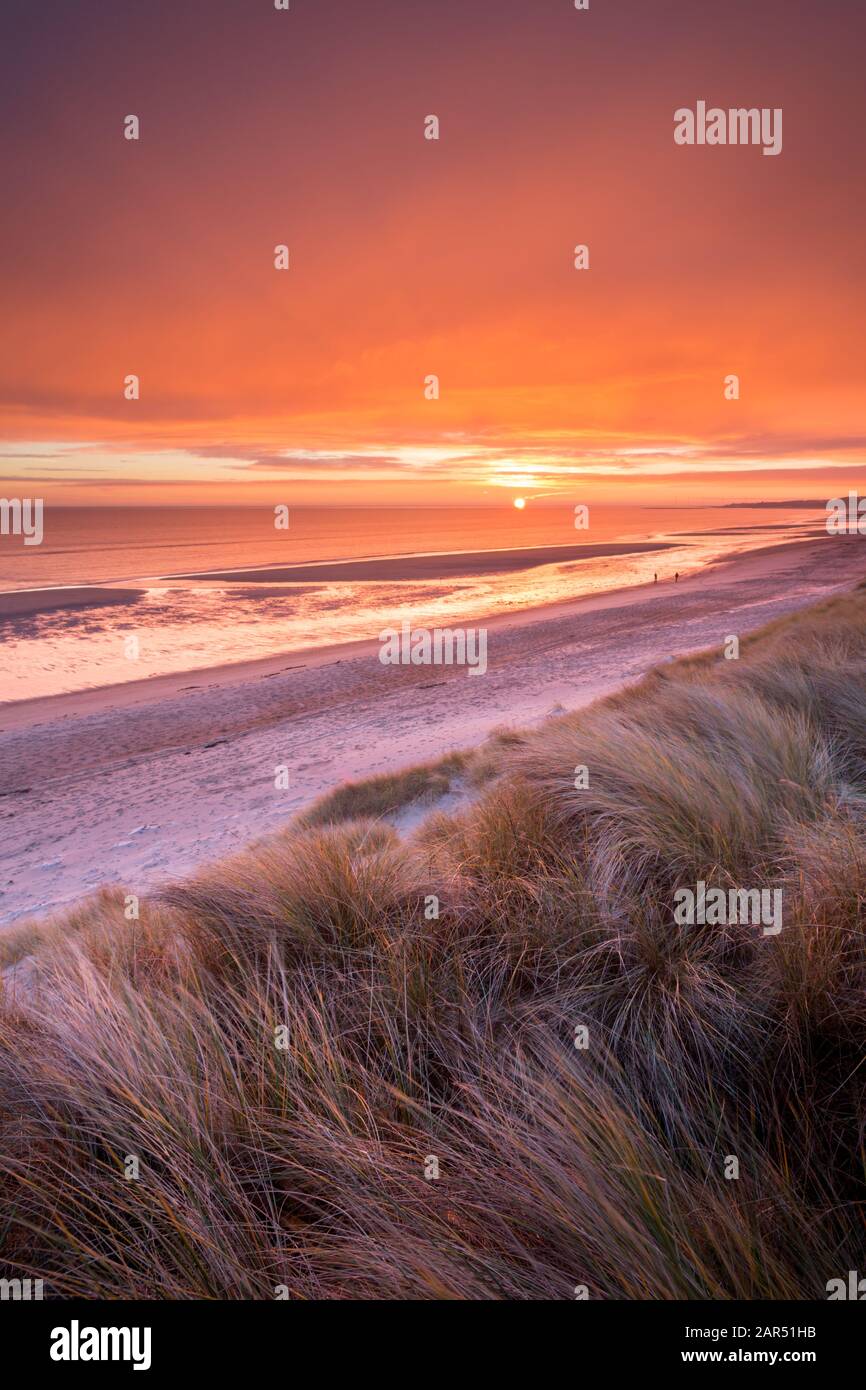 Ein lebendiger, leuchtend orangefarbener Sonnenaufgang von den Sanddünen über dem Strand der Druridge Bay und der Nordsee an der Northumberland-Küste im Winter. Stockfoto