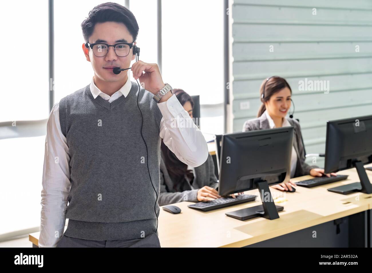 Portrait von jungen Erwachsenen freundlich und Vertrauen Betreiber Mann mit Headsets und sein Team arbeiten in einem Call Center, Kundendienst und technischen Sup Stockfoto