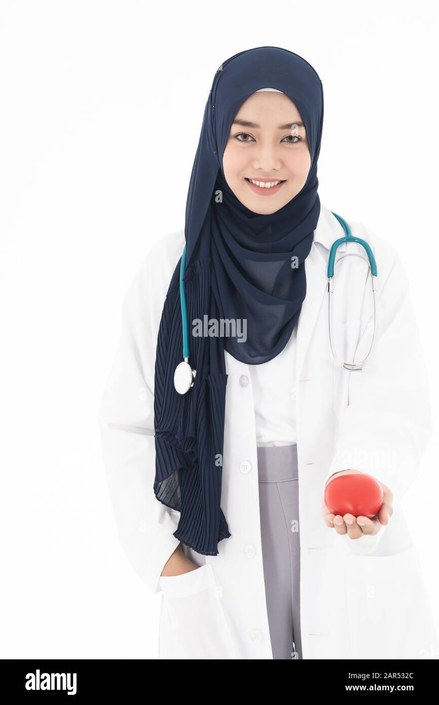 Asiatischer junger Erwachsener attraktiver muslimischer Frauenarzt, der mit Stethoskop stehend Hijab trägt und rotes Herz in weißem Hintergrund isoliert hält. Healthcar Stockfoto