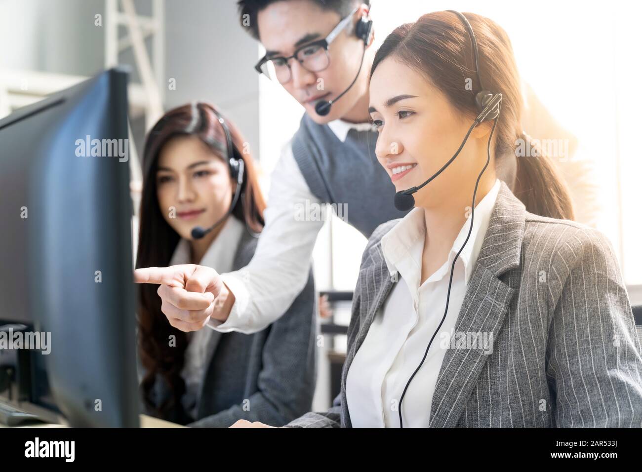 Jungen Erwachsenen vertrauen mit lächelnden Supervisor Lehre zu sein Team von operator Team Agent mit Headsets und Desktop Computer in einem Call Center zu Moni Stockfoto