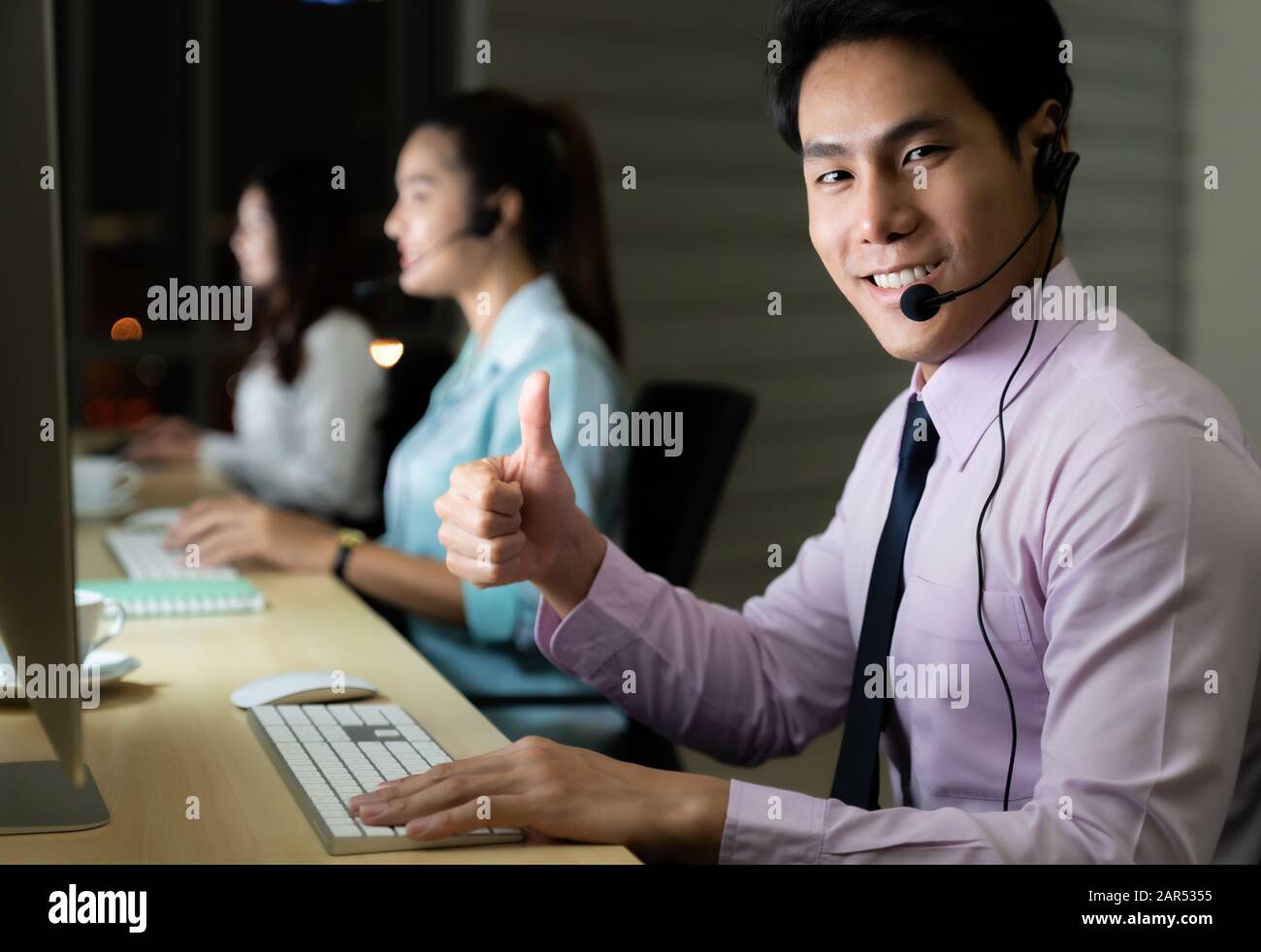 Asiatische junge Erwachsene vertrauen Betreiber mann Agent mit Headsets, die in einem Call Center bei Nacht Umwelt mit seinem Kollegen Team als Customer Servic Stockfoto