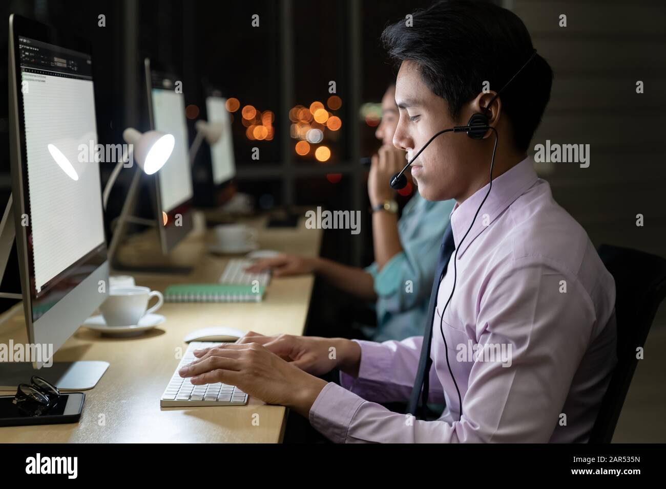 Asiatische junge Erwachsene vertrauen Betreiber mann Agent mit Headsets, die in einem Call Center bei Nacht Umwelt mit seinem Kollegen Team als Customer Servic Stockfoto