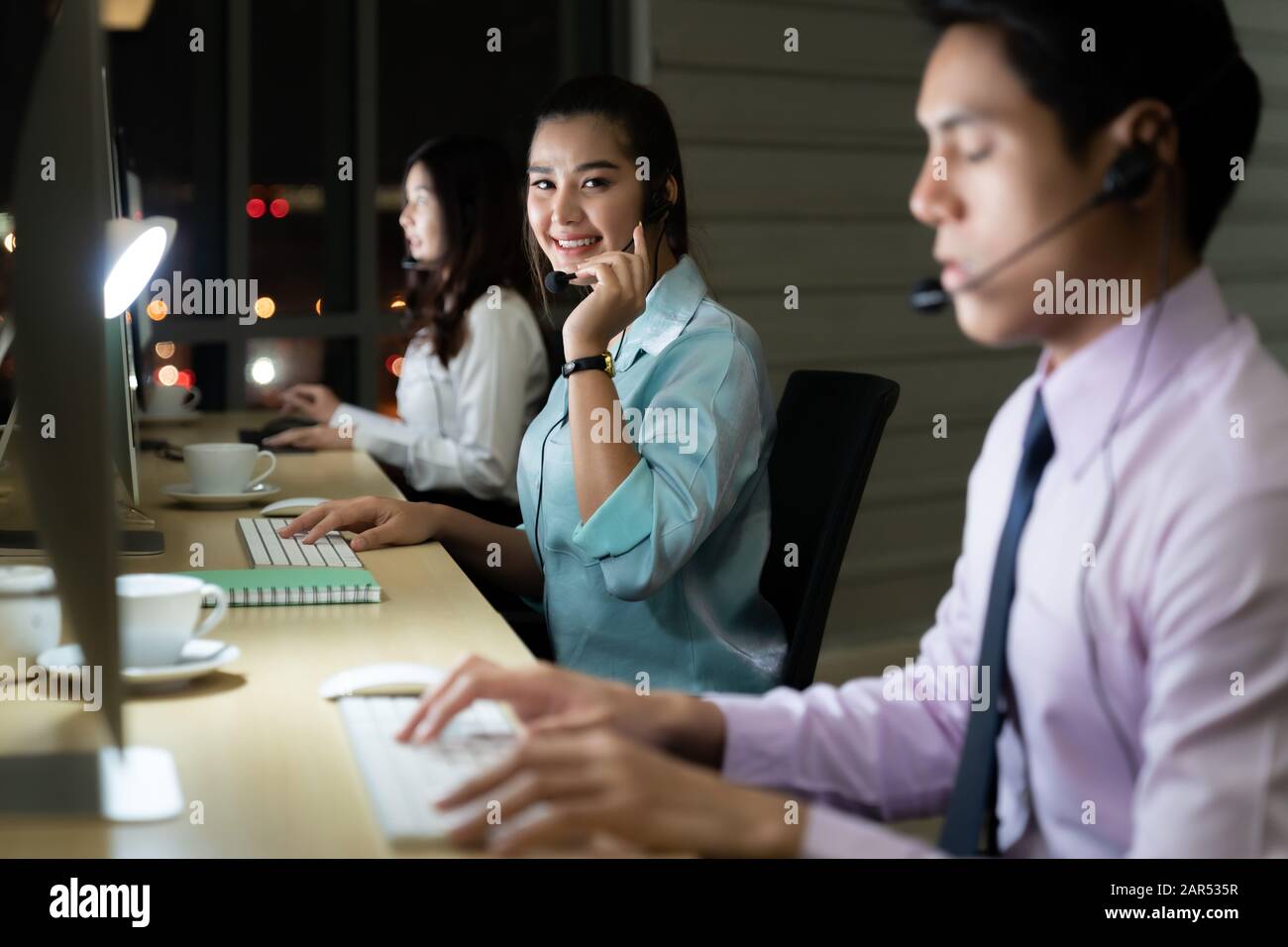 Asiatische junge Erwachsene vertrauen Betreiber Frau Agent mit Headsets, die in einem Call Center bei Nacht Umwelt mit seinem Kollegen Team als Kunde serv Stockfoto