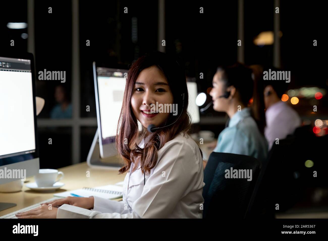 Asiatische junge Erwachsene vertrauen Betreiber Frau Agent mit Headsets, die in einem Call Center bei Nacht Umwelt mit seinem Kollegen Team als Kunde serv Stockfoto