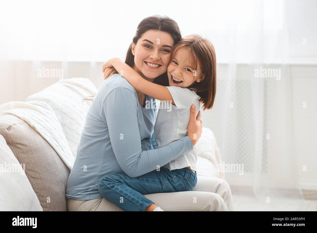 Kleine Tochter und junge Mutter umarmen sich zu Hause Stockfoto