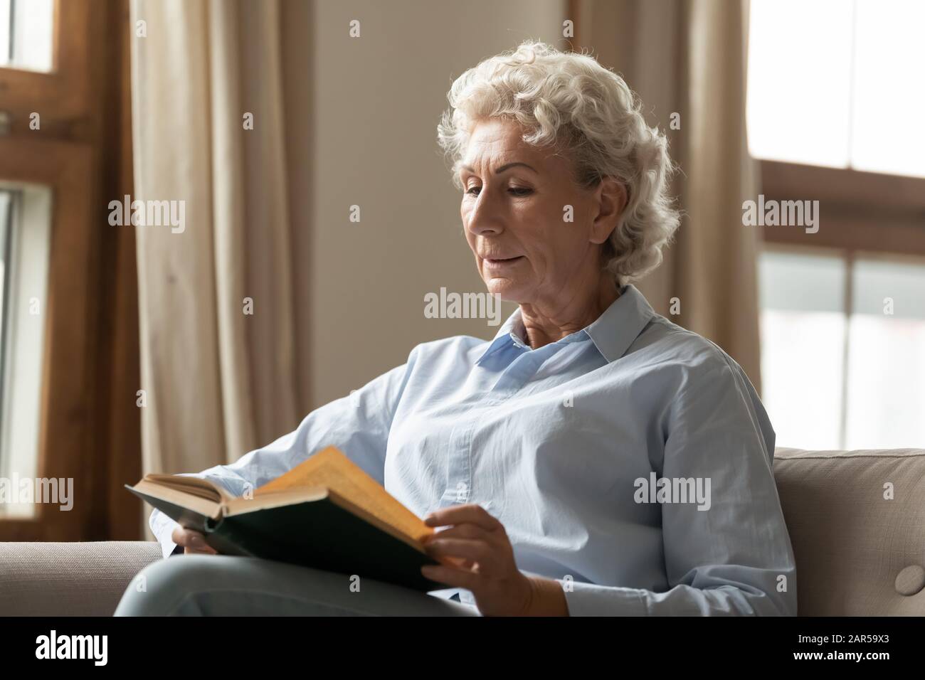 Friedliche Frau mittleren Alters liest Papierbuch-Bestseller zu Hause. Stockfoto