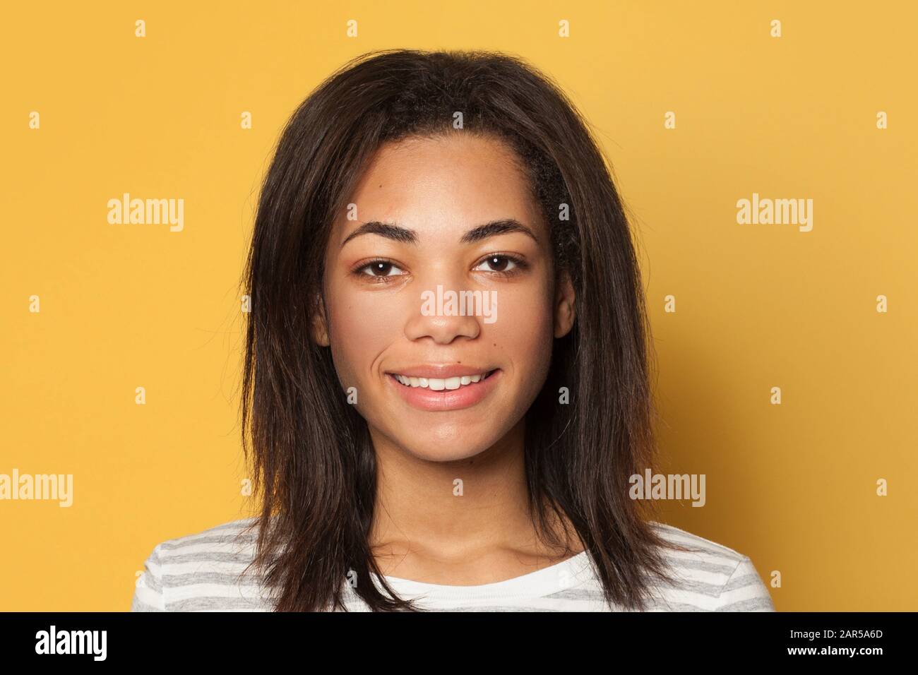 Fröhliche schöne brünette junge dunkelhäutige Frau auf gelbem Hintergrund, Studio-Porträt Stockfoto