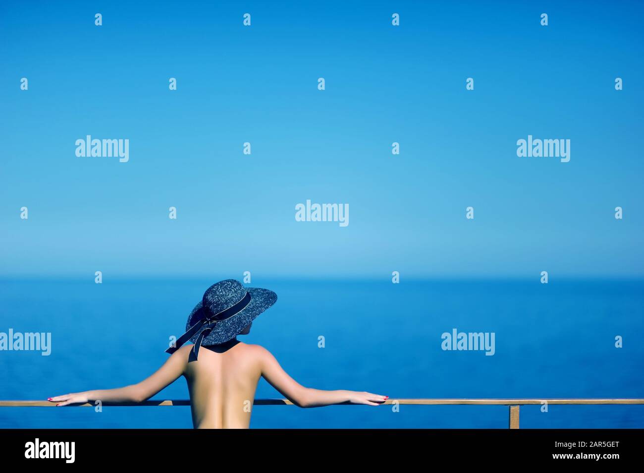 Mädchen in schwarzem Hut steht am Geländer auf dem Dach des Hotels und blickt auf den Horizont Stockfoto