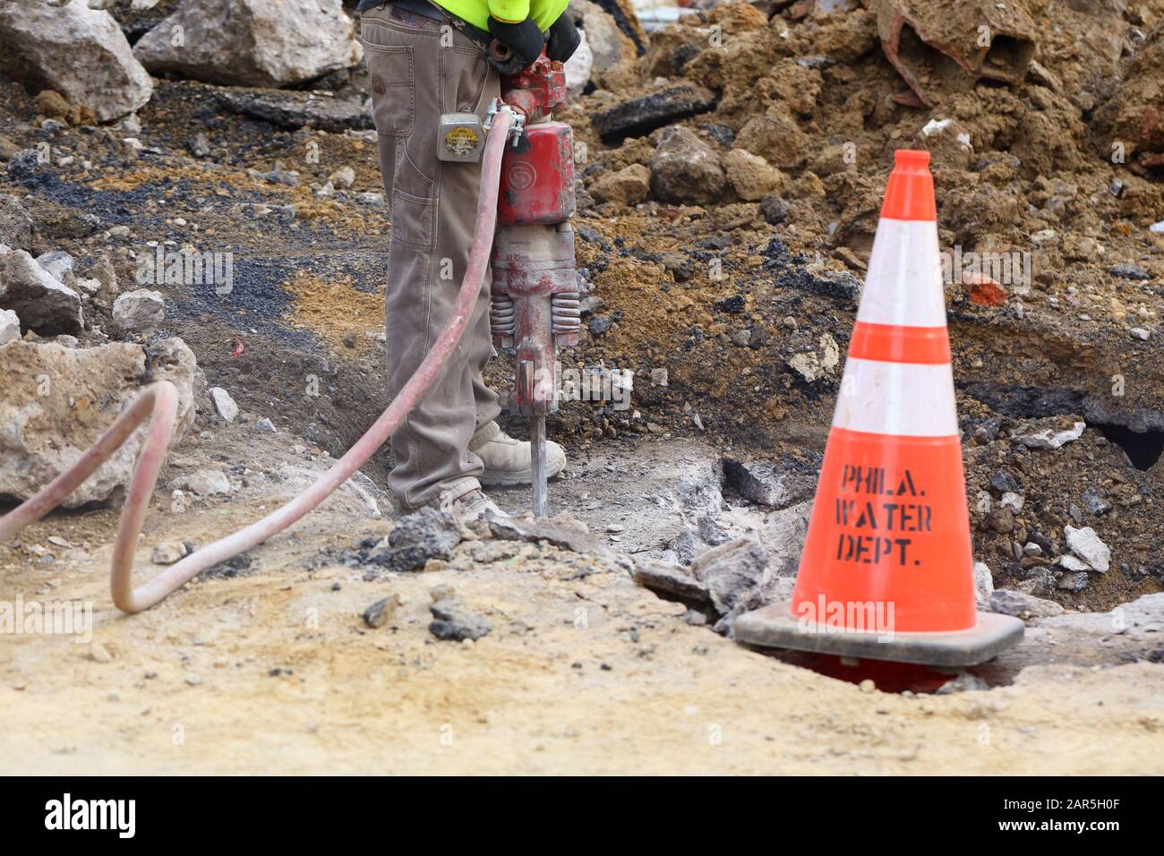 Ein Bauarbeiter des Wasserministeriums von Philadelphia betreibt einen Presslufthammer, um eine Straße zu öffnen, um eine Wasserleitung zu reparieren. Stockfoto