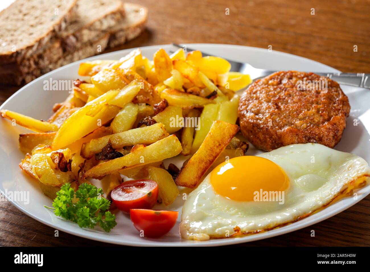 Pommes mit frittiertem Ei und einem großen Fleischball auf dem Teller Stockfoto