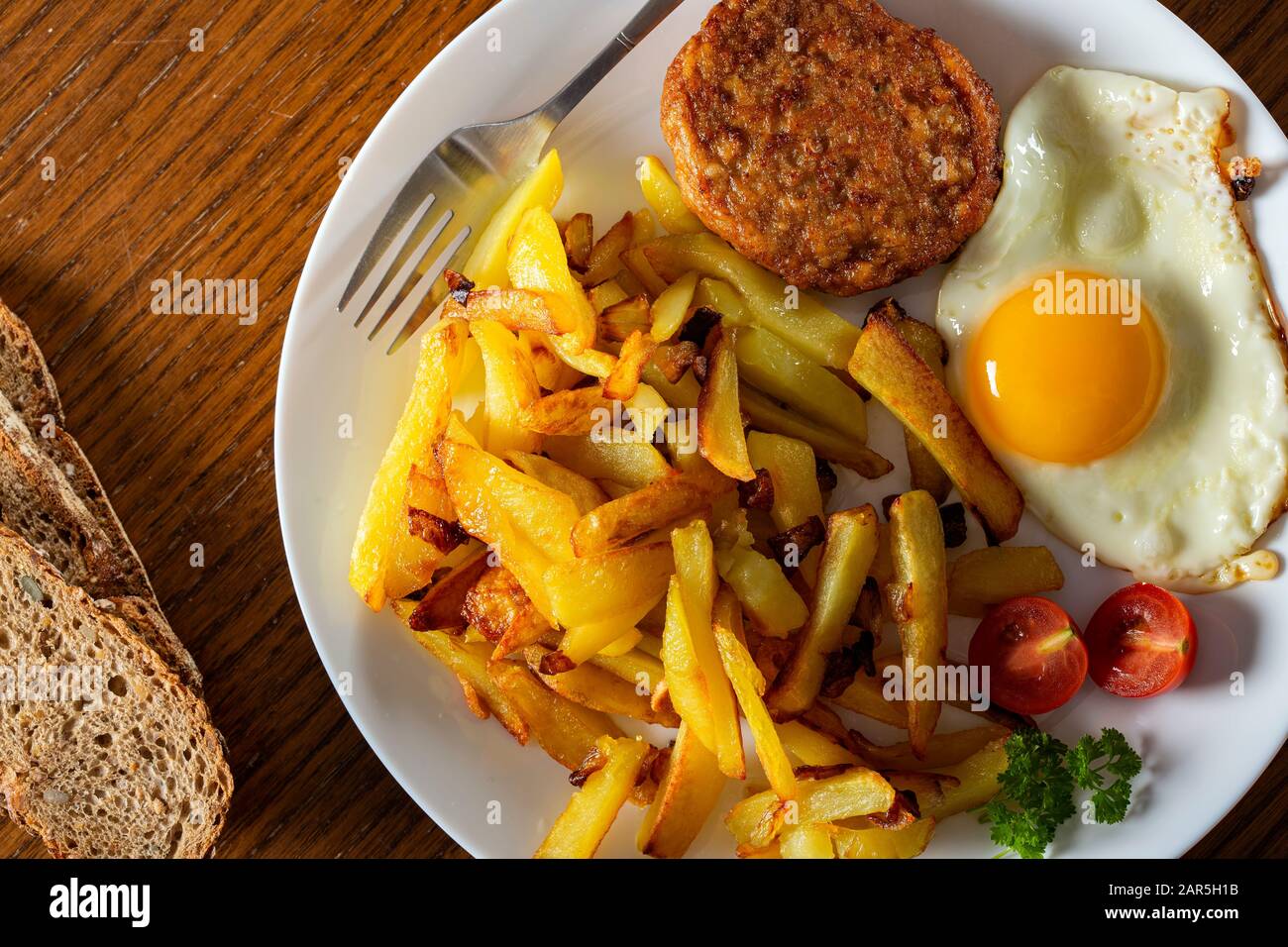 Pommes mit frittiertem Ei und einem großen Fleischball auf dem Teller - Draufsicht Stockfoto