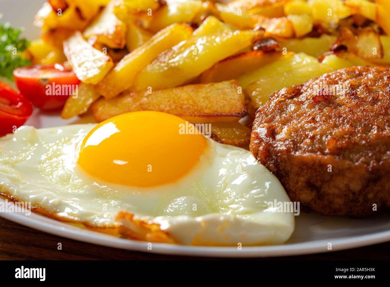 Pommes mit frittiertem Ei und einem großen Fleischball auf dem Teller - Nahansicht Stockfoto