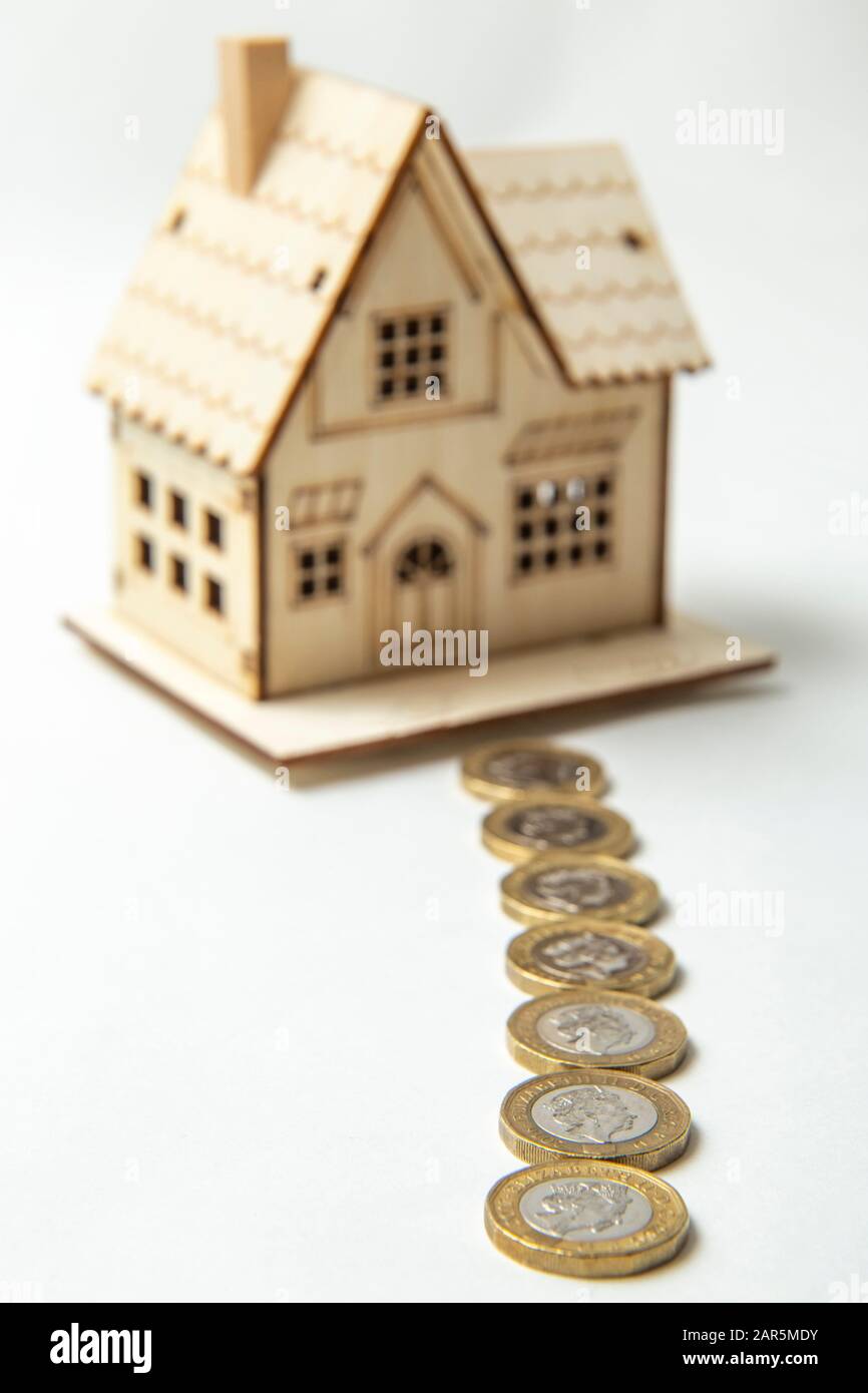 Pfad der Münzen, die zu einem Spielzeughaus führen. "House Out of Focus", die Münzen stehen im Vordergrund. Weißer Hintergrund. Stockfoto