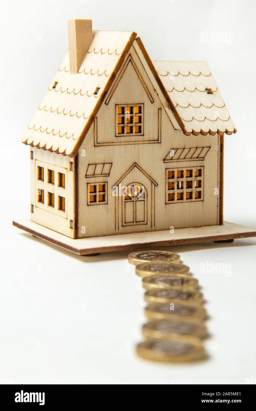 Pfad der Münzen, die zu einem Spielzeughaus führen. Haus im Fokus, fokussiert. Weißer Hintergrund. Stockfoto