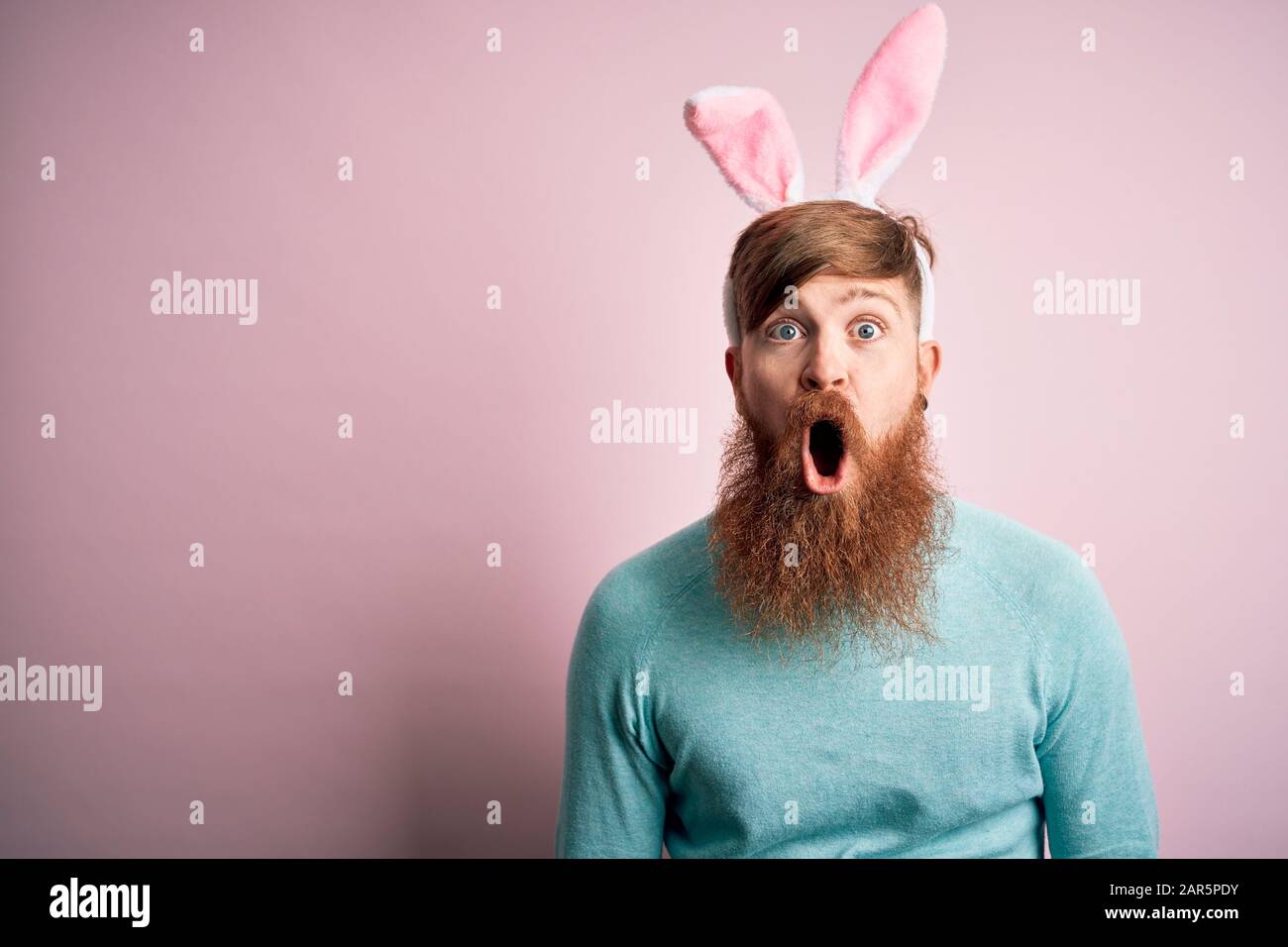 Hipster irischer Mann mit Bart, der Osterkaninchen-Ohren über isoliertem rosafarbenem Hintergrund trägt, fürchtet und schockiert mit Überraschungsausdruck, Angst und aufgeregter FA Stockfoto