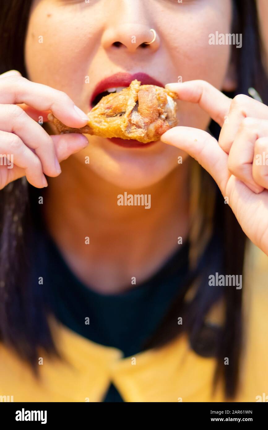 Junge Frau, die Hühnerflügel mit den Händen isst Stockfoto