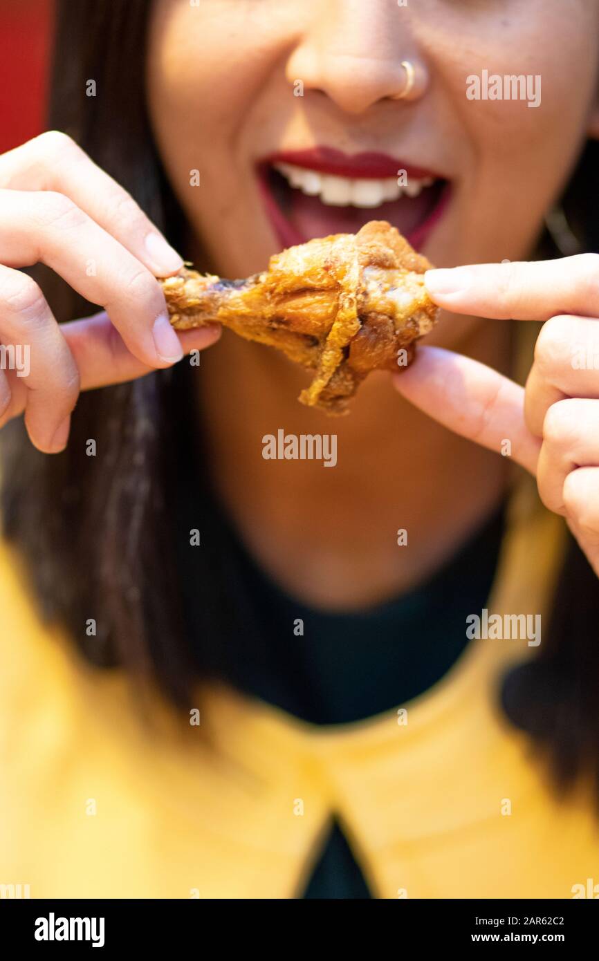Junge Frau, die Hühnerflügel mit den Händen isst Stockfoto