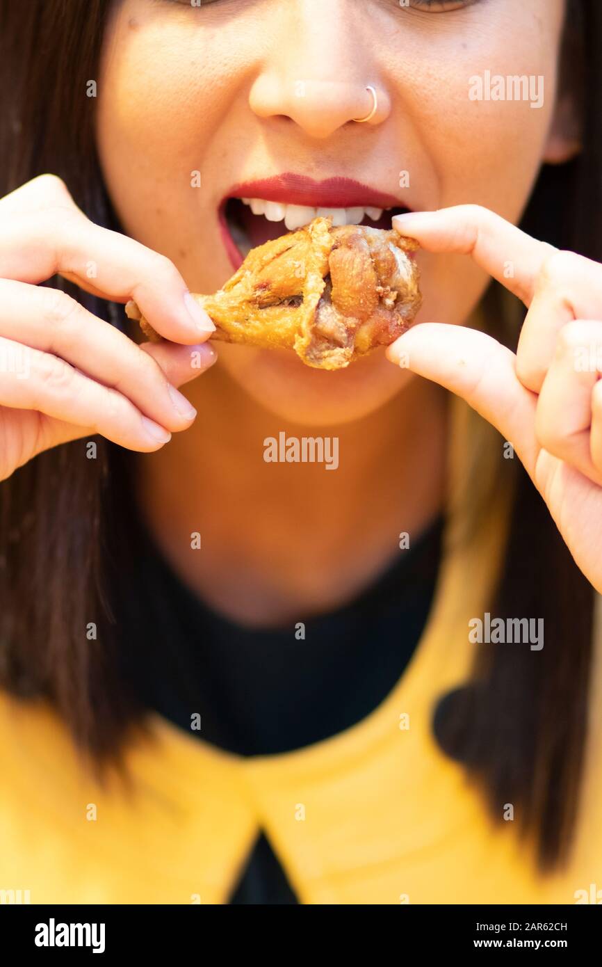 Junge Frau, die Hühnerflügel mit den Händen isst Stockfoto