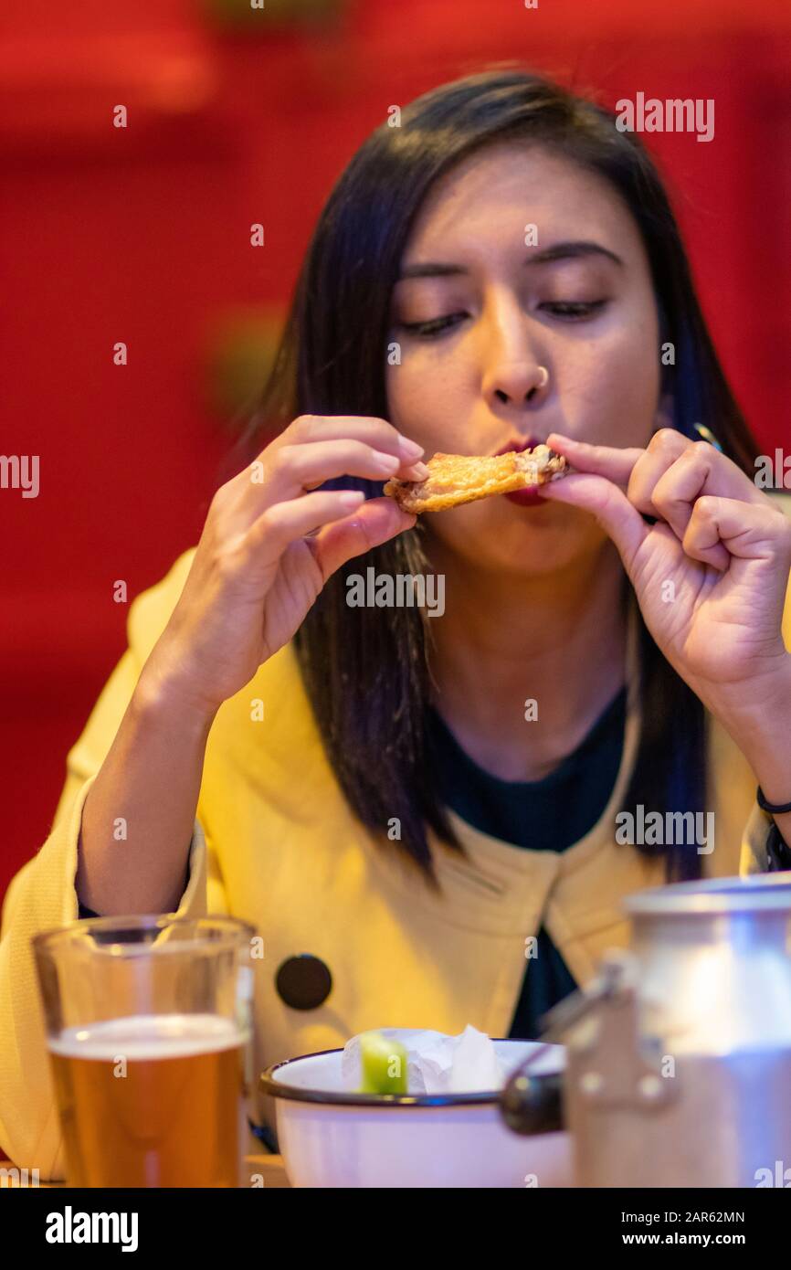 Junge Frau, die Hühnerflügel mit den Händen isst Stockfoto