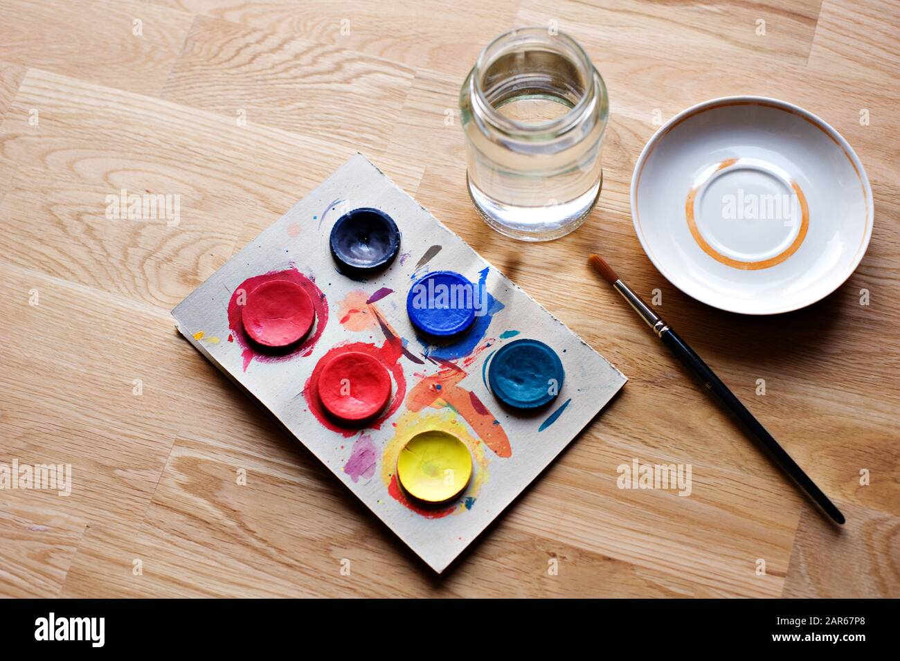 Aquarellfarben mit Pinsel, Platte und Glasbecher auf dem Holztisch. Stockfoto