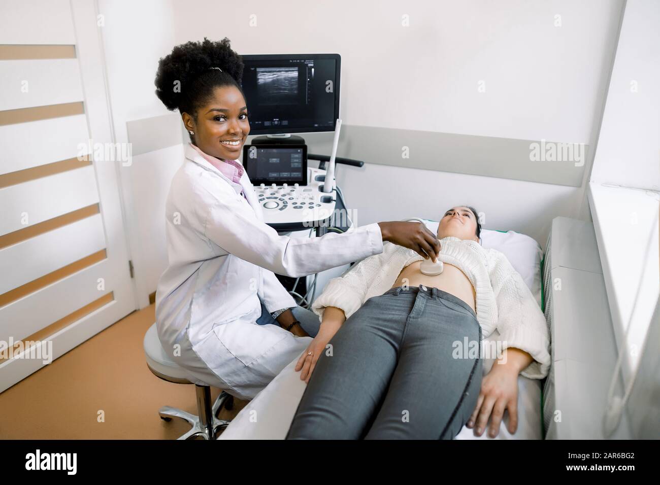 Junge schwarze Frau Arzt Sonograph mit Ultraschallgerät bei der Arbeit, mit dem Ultraschall-Scanner in der Hand halten, während die weiblichen Patienten Abdomen bei untersuchen Stockfoto