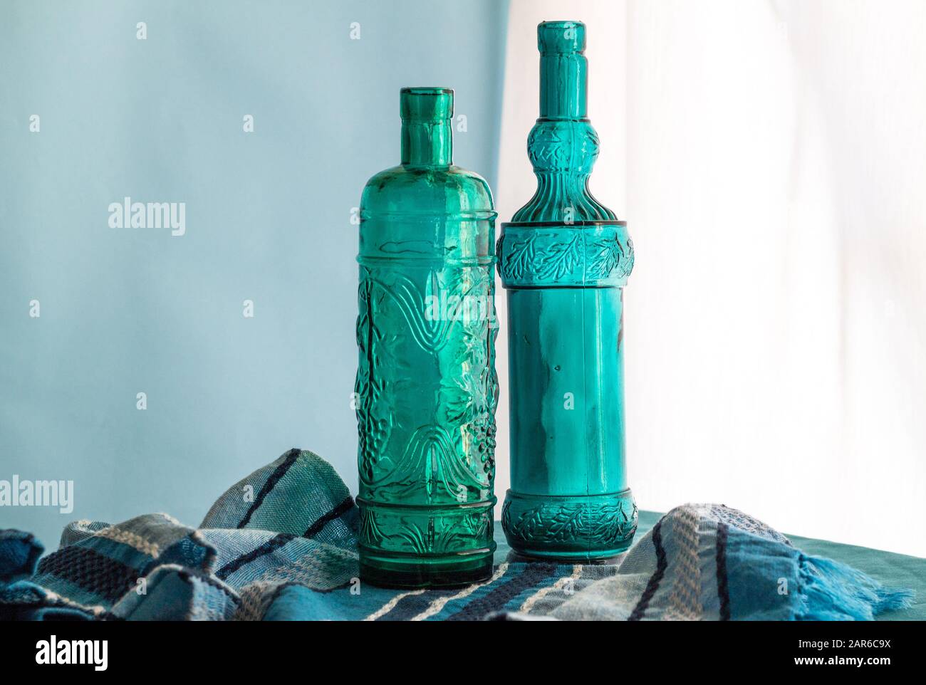 Weinflaschen Stillleben mit zwei handgefertigten, blauen Glasflaschen aus recyceltem spanischem Glas vor dem Fenster - horizontales Bild mit s Stockfoto