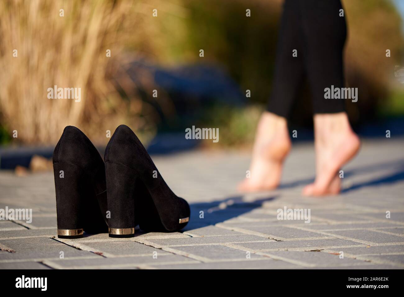 Schwarze Schuhe auf der Straße auf einem Hintergrund barfuß weibliche Beine. Stockfoto