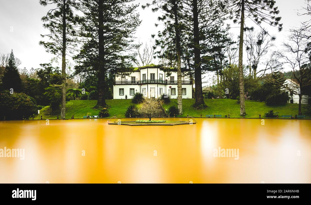 Gelbes Wasserbecken mit Seideneffekt und großem Haus hinten Stockfoto