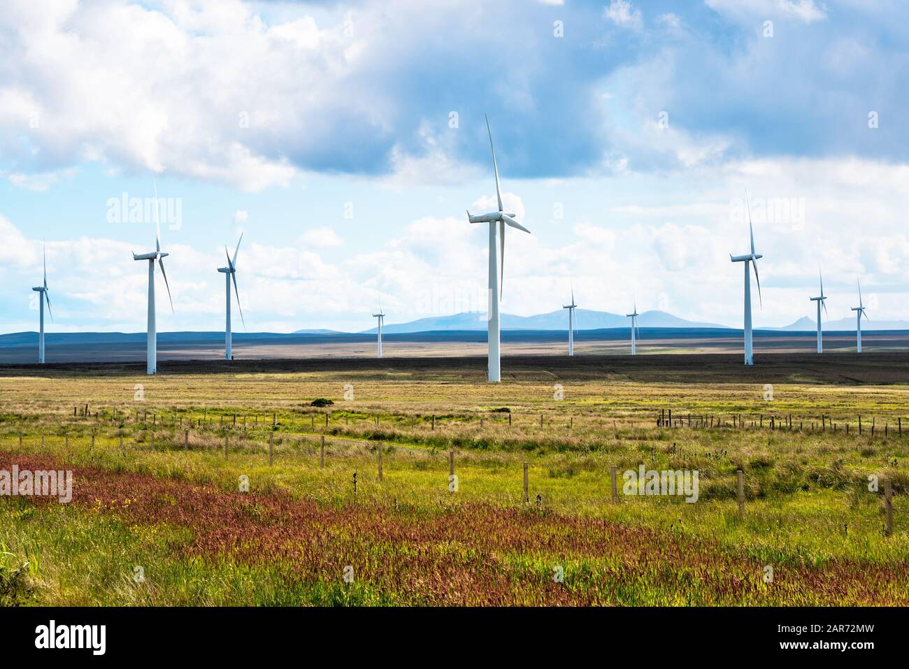 Windkraftanlagen in einem grasbewachsenen Feld mit Bergen am Horizont an einem teilweise bewölkten Frühlingstag Stockfoto