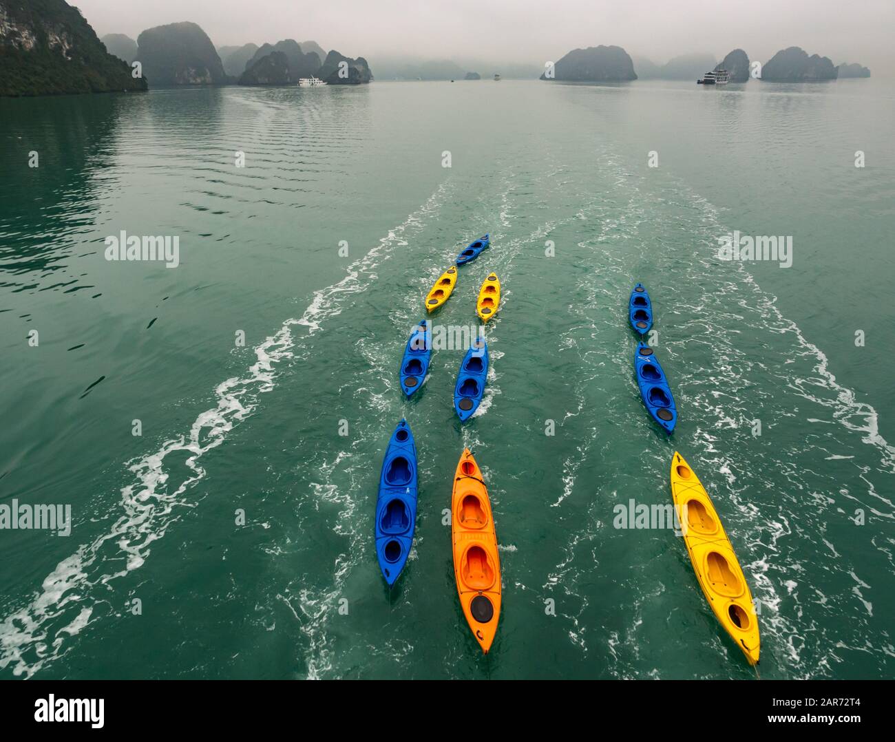 Kajaks, die von einem Kreuzfahrtschiff mit Kalkkarsthügeln bei nebelartigem Wetter, Halong Bay, Vietnam, Asien, gezogen werden Stockfoto