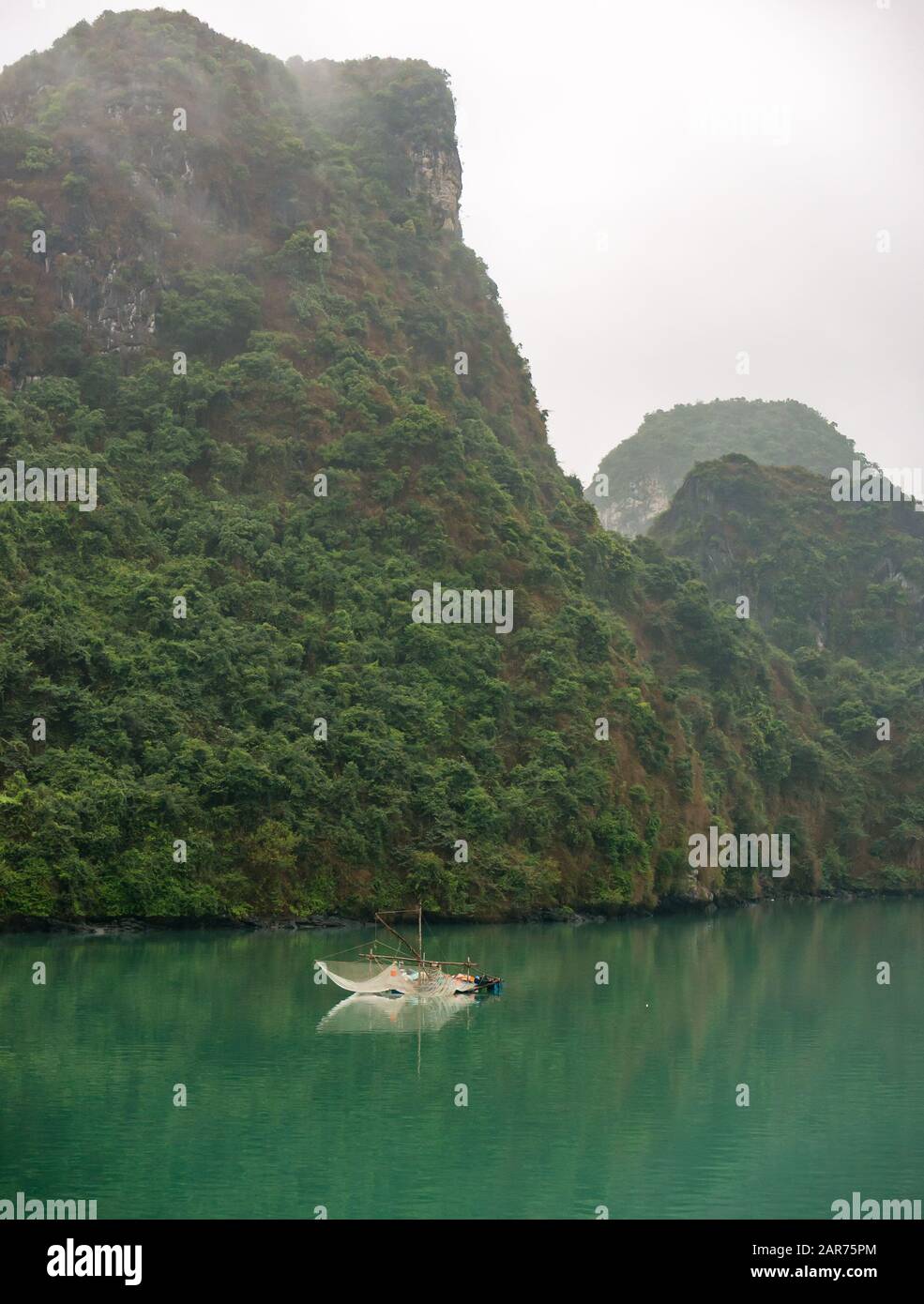 Traditionelles Fischerboot mit Netzen bei nebligen Wetter mit Kalkfelskarstklippen, Lan ha Bay, Vietnam, Asien Stockfoto