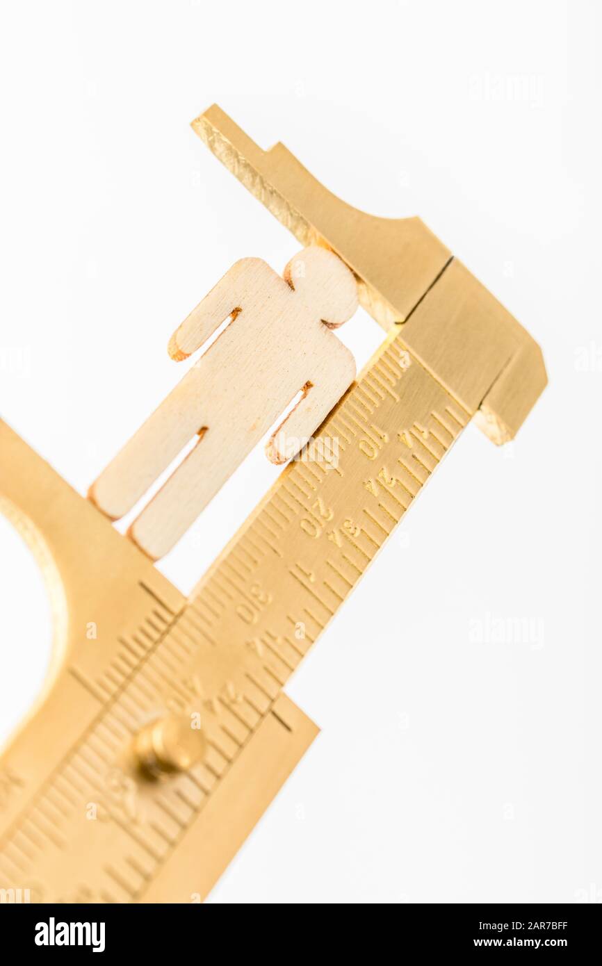 Makro kleine lasergeschnittene Holzfigur und Messing-Zirkel gegen den weißlichen BG. Messung von persönlichen Leistungsindikatoren, demografischen Daten, Produktivität, Stockfoto