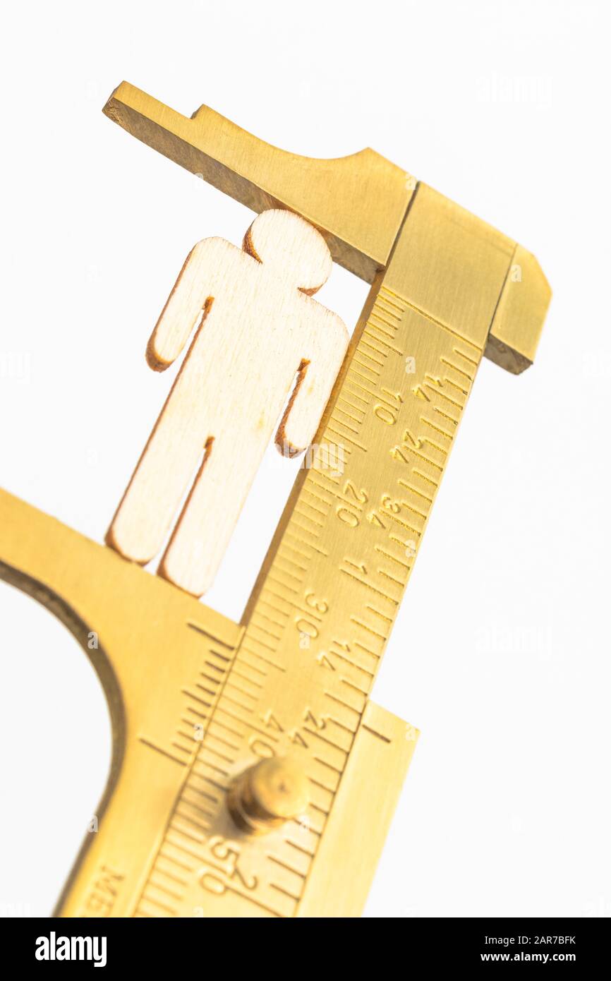 Makro kleine lasergeschnittene Holzfigur und Messing-Zirkel gegen den weißlichen BG. Messung von persönlichen Leistungsindikatoren, demografischen Daten, Produktivität, Stockfoto